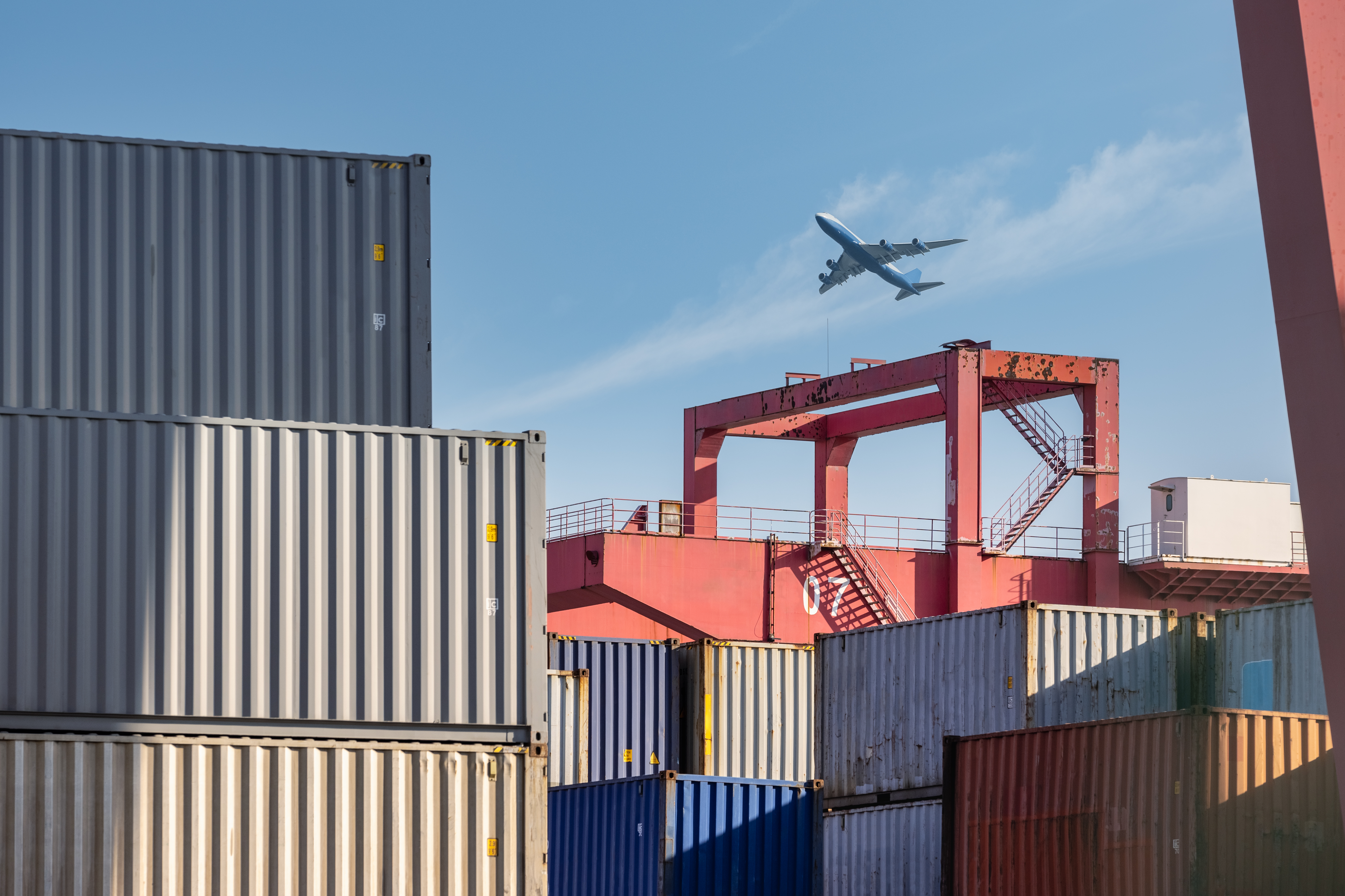 container-yard-closeup-with-airplane-in-sky-2023-11-27-04-50-06-utc
